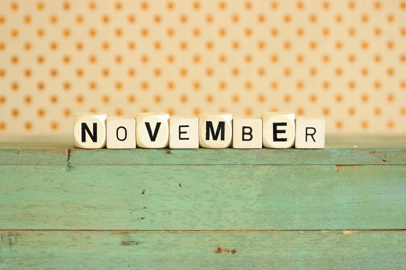 Image of word November on a fun green table with polka dot background.