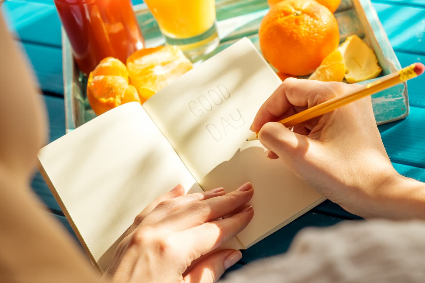 woman writing good day in a book with tray of citrus